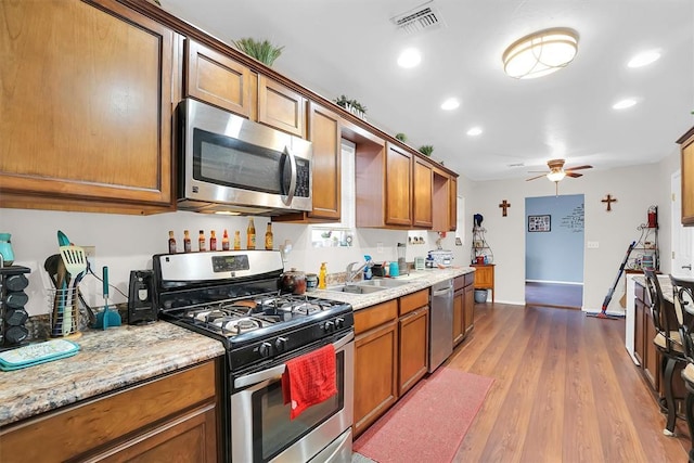 kitchen with sink, light wood-type flooring, ceiling fan, stainless steel appliances, and light stone countertops