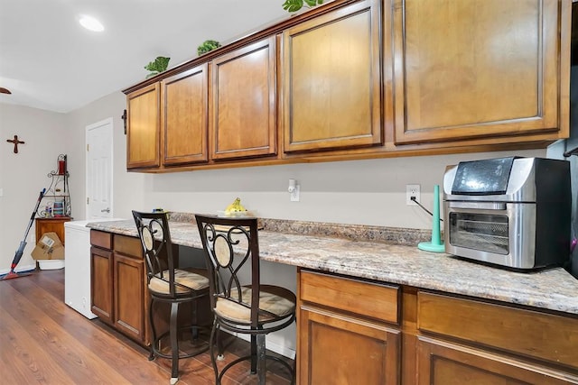 kitchen with hardwood / wood-style floors, light stone countertops, and built in desk