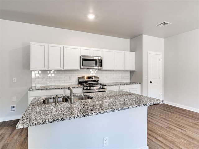 kitchen with appliances with stainless steel finishes, dark hardwood / wood-style floors, sink, white cabinets, and a center island with sink