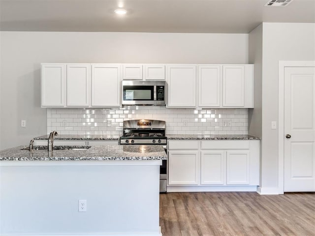 kitchen featuring stainless steel appliances, white cabinetry, sink, and light stone counters