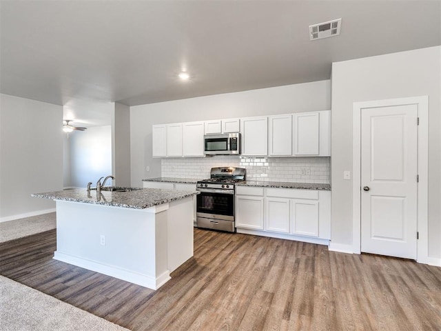 kitchen with appliances with stainless steel finishes, sink, white cabinets, light stone countertops, and light wood-type flooring