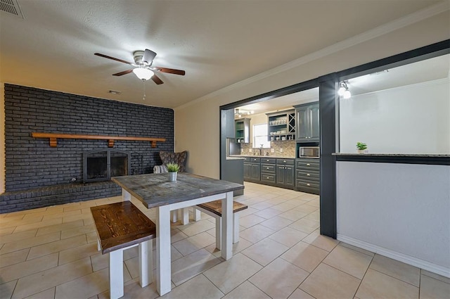 dining area with a textured ceiling, ceiling fan, ornamental molding, a brick fireplace, and light tile patterned floors