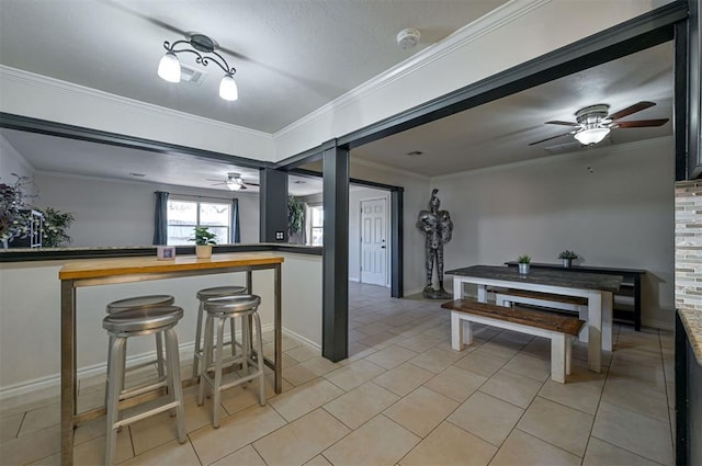 kitchen with ceiling fan, butcher block countertops, a breakfast bar, light tile patterned flooring, and crown molding