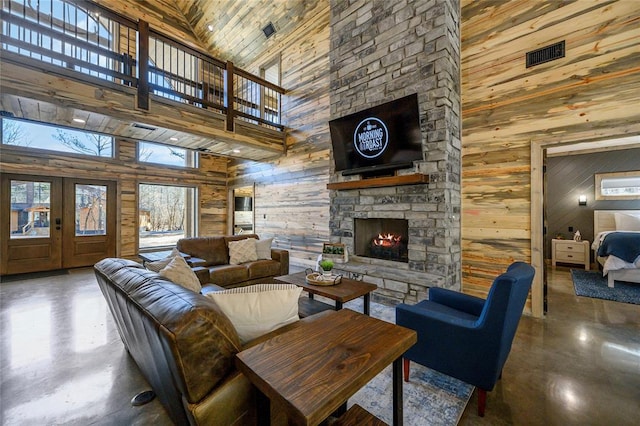 living room featuring french doors, a stone fireplace, concrete flooring, and wood walls