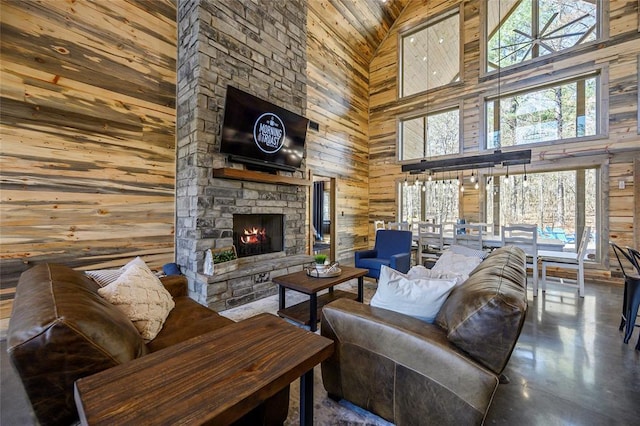 living room featuring concrete flooring, wood walls, a high ceiling, and a stone fireplace