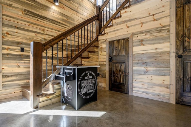 staircase with a high ceiling, concrete flooring, and wood walls