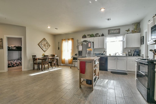 kitchen with black appliances, a kitchen island, a wealth of natural light, and white cabinets