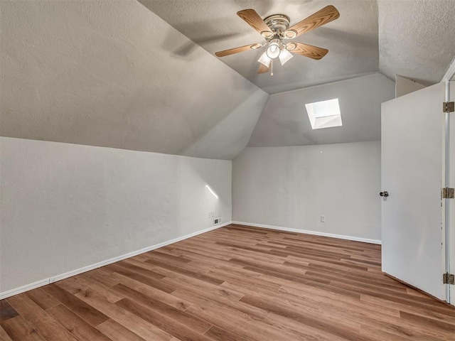 additional living space featuring ceiling fan, vaulted ceiling with skylight, a textured ceiling, and light hardwood / wood-style floors