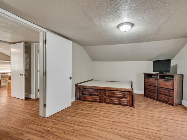 bedroom featuring vaulted ceiling, a textured ceiling, and light hardwood / wood-style flooring