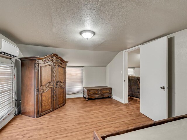 interior space with lofted ceiling, a wall mounted AC, plenty of natural light, a textured ceiling, and light wood-type flooring