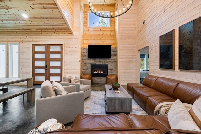 living room with a high ceiling, a fireplace, concrete floors, wood walls, and an inviting chandelier