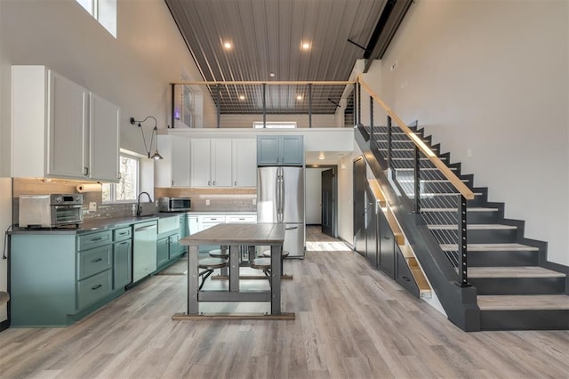 kitchen featuring light hardwood / wood-style floors, white cabinets, stainless steel appliances, and a towering ceiling