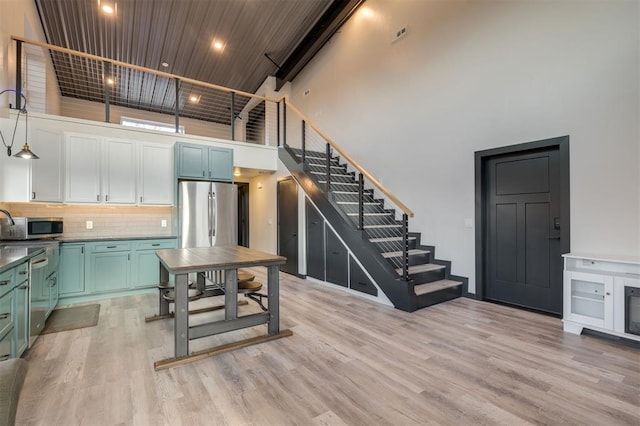 kitchen with light hardwood / wood-style floors, appliances with stainless steel finishes, a high ceiling, pendant lighting, and backsplash