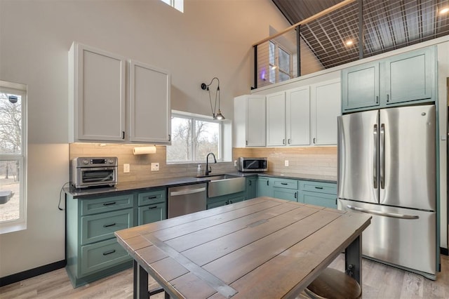 kitchen with a high ceiling, white cabinets, appliances with stainless steel finishes, and light hardwood / wood-style floors