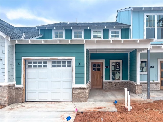 view of front facade featuring covered porch, a shingled roof, concrete driveway, stone siding, and board and batten siding