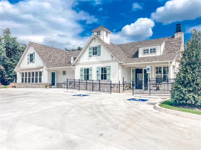 back of property with a fenced front yard, stone siding, roof with shingles, board and batten siding, and a chimney