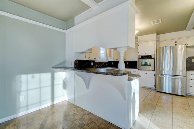 kitchen featuring light parquet floors, appliances with stainless steel finishes, white cabinetry, tasteful backsplash, and kitchen peninsula