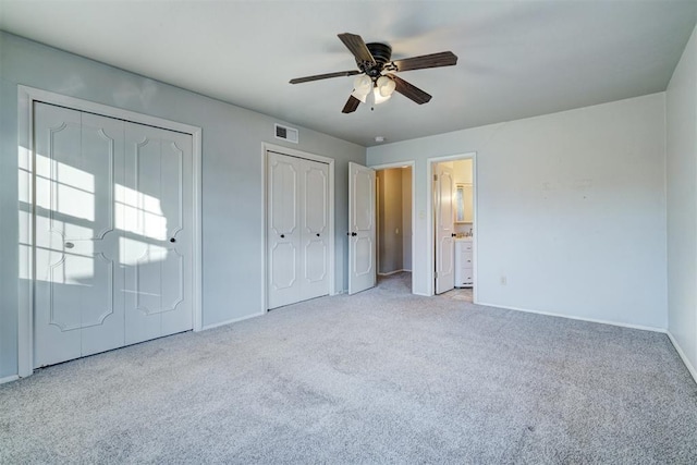 unfurnished bedroom with multiple closets, light colored carpet, connected bathroom, and ceiling fan