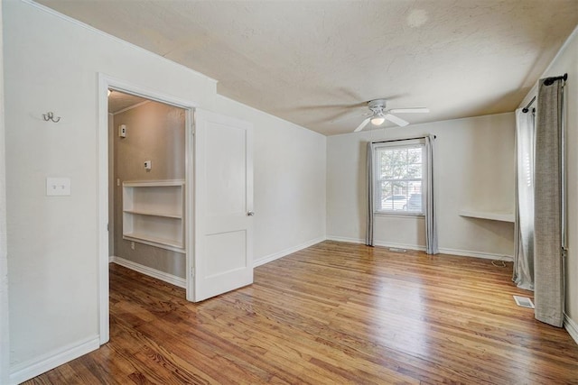 unfurnished room with hardwood / wood-style floors, built in shelves, and ceiling fan