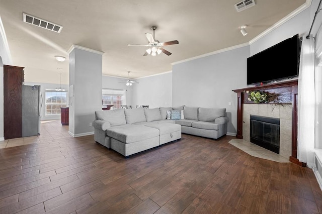 living room featuring a tile fireplace, hardwood / wood-style floors, ceiling fan, and crown molding