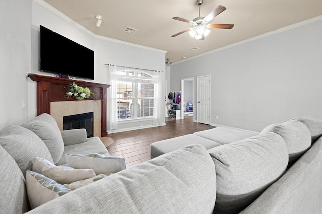 living room with a tiled fireplace, hardwood / wood-style floors, crown molding, and ceiling fan