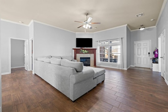 living room with a tiled fireplace, ornamental molding, and ceiling fan