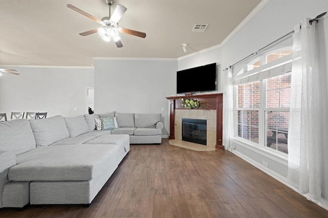 living room featuring a tile fireplace, wood-type flooring, ceiling fan, and crown molding