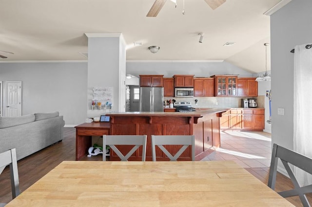 kitchen featuring a breakfast bar, ceiling fan, backsplash, stainless steel appliances, and ornamental molding