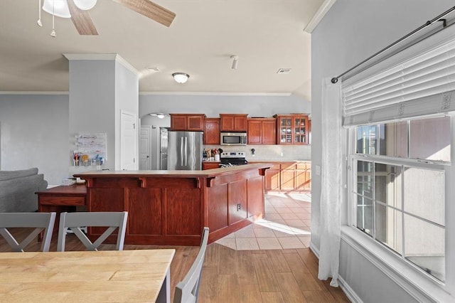 kitchen with stainless steel appliances, ornamental molding, a kitchen breakfast bar, and light hardwood / wood-style floors