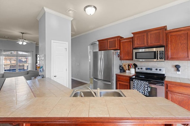 kitchen featuring appliances with stainless steel finishes, tasteful backsplash, sink, ornamental molding, and tile counters