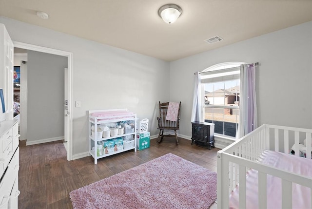 bedroom featuring dark hardwood / wood-style floors, a nursery area, and a wood stove