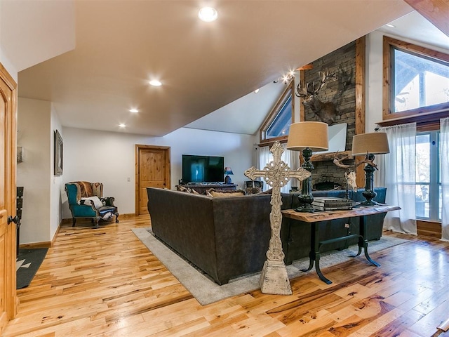 living room with light wood-type flooring, a stone fireplace, and lofted ceiling