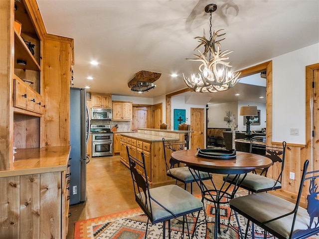 kitchen with appliances with stainless steel finishes, a chandelier, decorative backsplash, kitchen peninsula, and pendant lighting