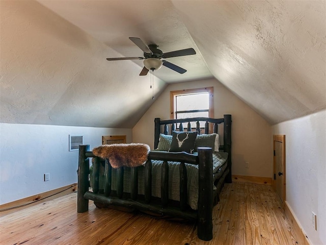 bedroom featuring ceiling fan, light hardwood / wood-style floors, a textured ceiling, and lofted ceiling