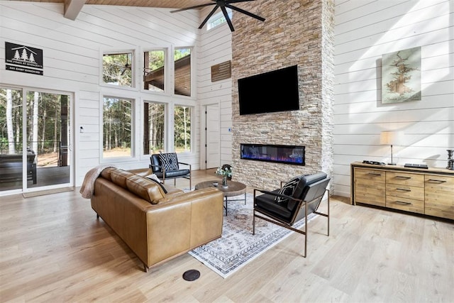 living room featuring high vaulted ceiling, a fireplace, light wood-type flooring, wood ceiling, and beam ceiling