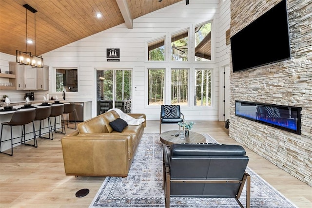 living room with a stone fireplace, a wealth of natural light, high vaulted ceiling, and beamed ceiling