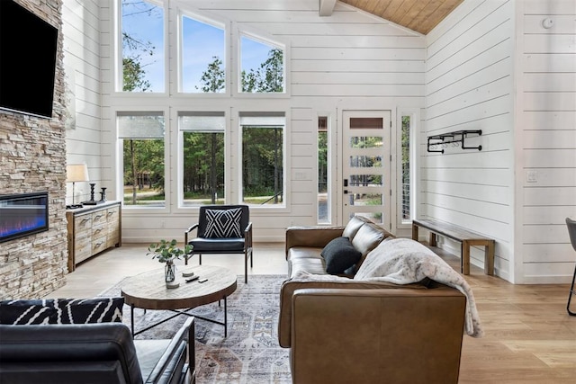 living room with wood ceiling, a stone fireplace, high vaulted ceiling, and light wood-type flooring