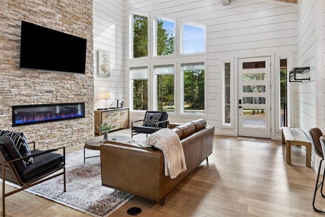 living room featuring a towering ceiling, a stone fireplace, and light wood-type flooring