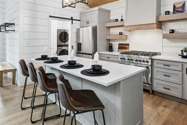 kitchen with stainless steel appliances, a barn door, gray cabinets, and stacked washer / drying machine