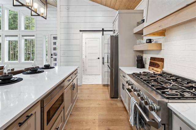 kitchen featuring light stone counters, light hardwood / wood-style flooring, stainless steel appliances, and a barn door