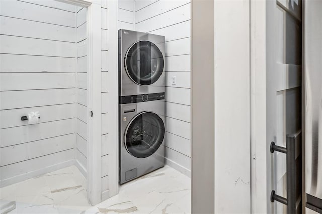 clothes washing area featuring stacked washer / drying machine and wood walls