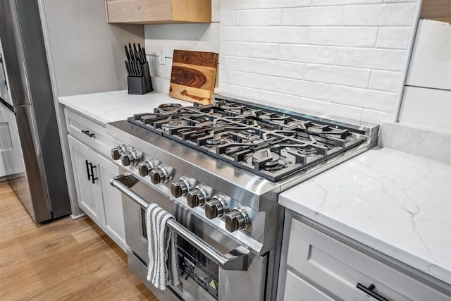 kitchen with light stone counters, appliances with stainless steel finishes, decorative backsplash, and light wood-type flooring