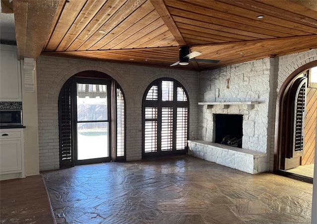 unfurnished living room with ceiling fan, plenty of natural light, a fireplace, and wood ceiling