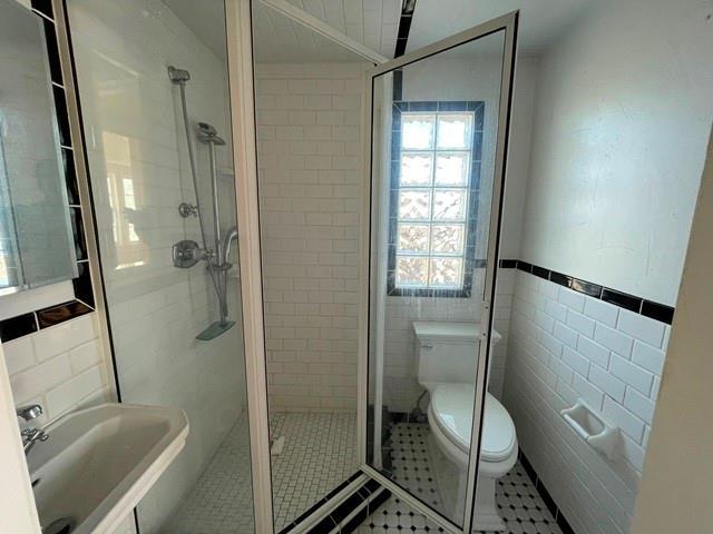 bathroom featuring sink, tile walls, a shower with shower door, tile patterned floors, and toilet