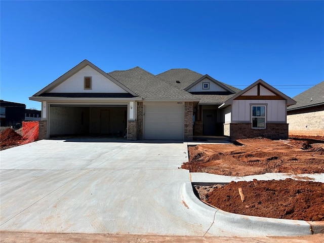 view of front of house with an attached garage, a shingled roof, concrete driveway, and brick siding