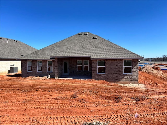 back of house featuring roof with shingles, central AC unit, and brick siding