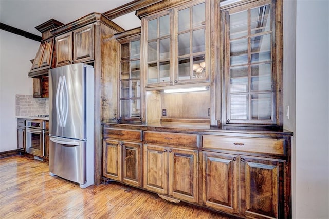 kitchen featuring crown molding, backsplash, light hardwood / wood-style floors, and appliances with stainless steel finishes