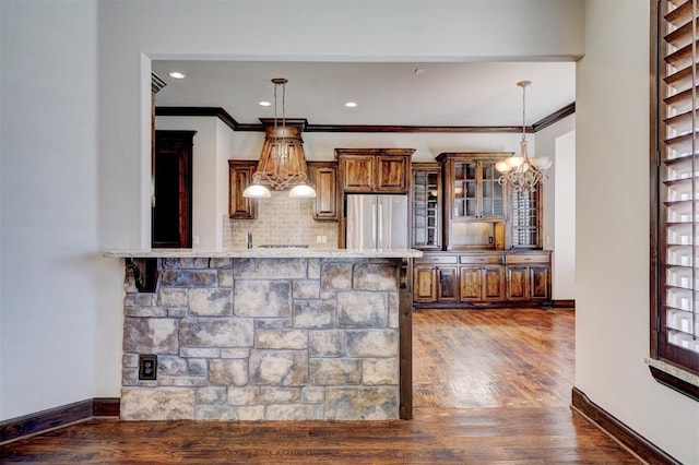 bar featuring decorative light fixtures, stainless steel refrigerator, ornamental molding, and decorative backsplash