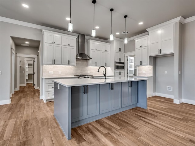 kitchen with hanging light fixtures, wall chimney exhaust hood, sink, white cabinets, and stainless steel oven