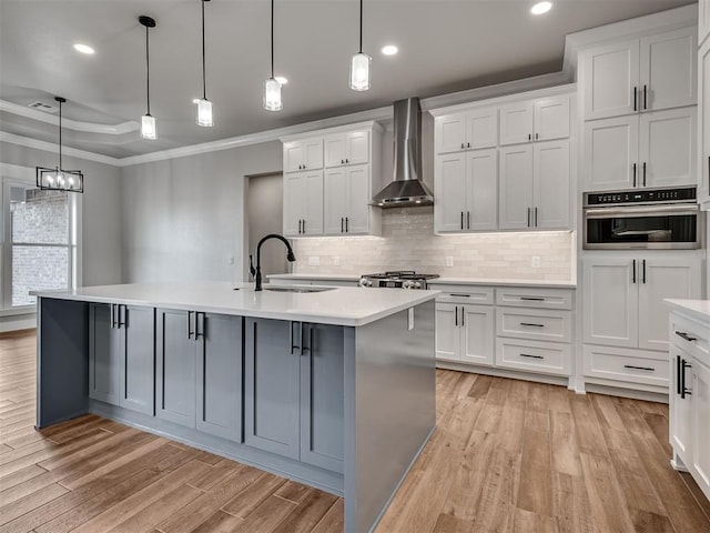 kitchen featuring sink, a kitchen island with sink, oven, and wall chimney range hood